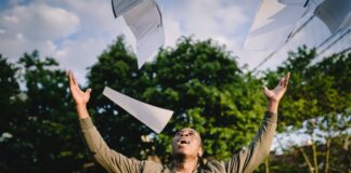 happy student throwing papers in air in park