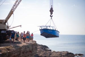 people transporting a boat on crane on rocky coast