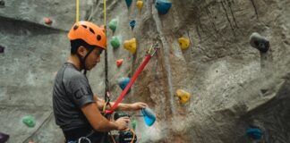 asian technician making hole in climbing hold with screwdriver while hanging on safety rope
