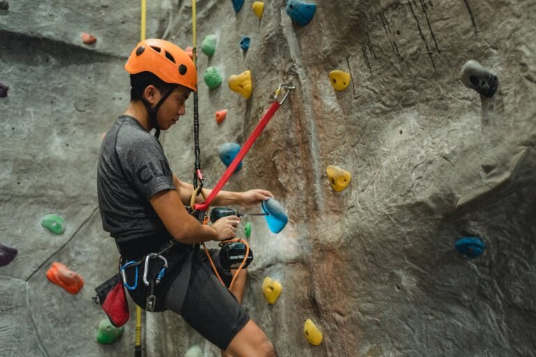asian technician making hole in climbing hold with screwdriver while hanging on safety rope