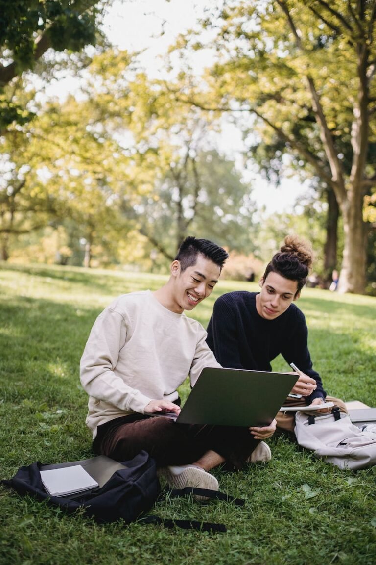 cheerful ethnic male students working on assignment on park lawn