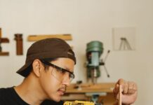 ethnic man in safety glasses drilling wooden plank