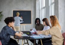 anonymous man writing on chalkboard near group of diverse students at table