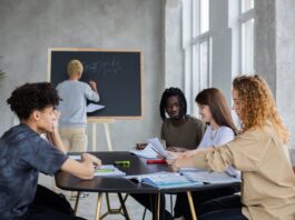 anonymous man writing on chalkboard near group of diverse students at table