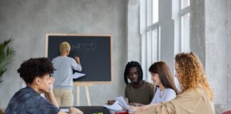anonymous man writing on chalkboard near group of diverse students at table