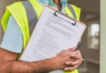 person in yellow reflective safety vest holding a pen and checklist of house inspection