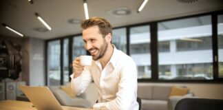 depth of field photo of man sitting on chair while holding cup in front of table