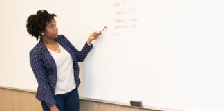 woman wearing black blazer holding pen pointing white marker board