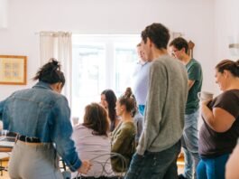 five people standing near four people sitting near desk