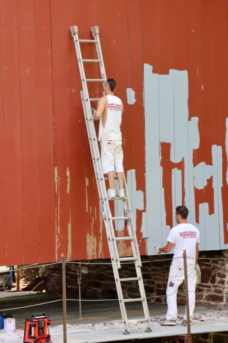 two men in white work uniforms using ladder to repaint a wooden wall