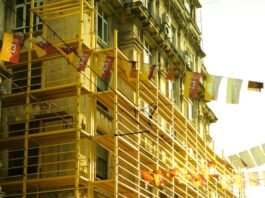people walking on a street by a building with scaffolding attached