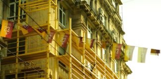 people walking on a street by a building with scaffolding attached