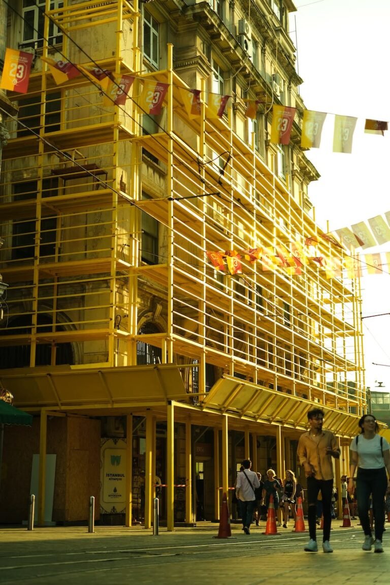 people walking on a street by a building with scaffolding attached