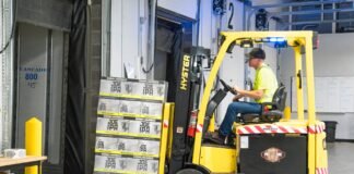 man riding a yellow forklift lifting boxes