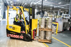 person driving yellow forklift carrying metal barrels