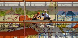 two person on scaffolding painting wall