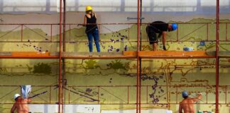 four people painting wall on scaffolding