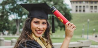 selective focus portrait photo of smiling woman in black academic dress holding diploma posing
