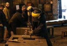 anonymous craftsman fixing metal construction while working in factory with colleagues