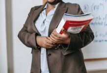 anonymous black female tutor with books standing near whiteboard at school