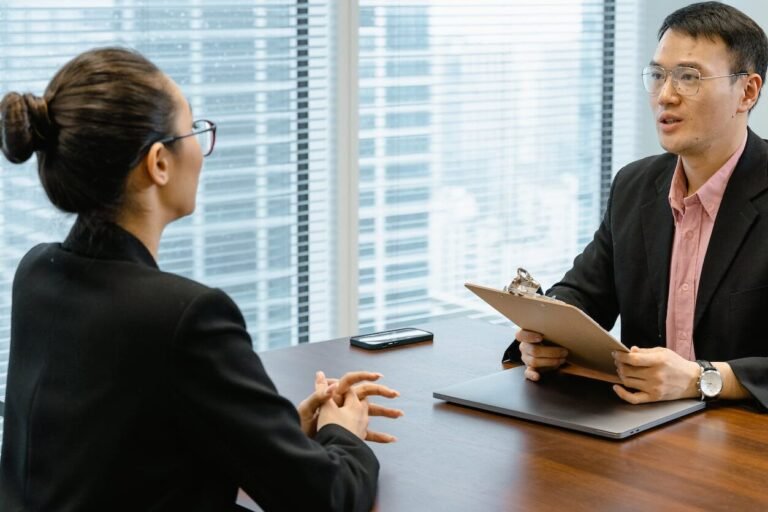 man in glasses holding a folder while talking to a woman in suit