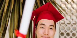 a man wearing red toga and graduation cap holding a rolled certificate while smiling at the camera