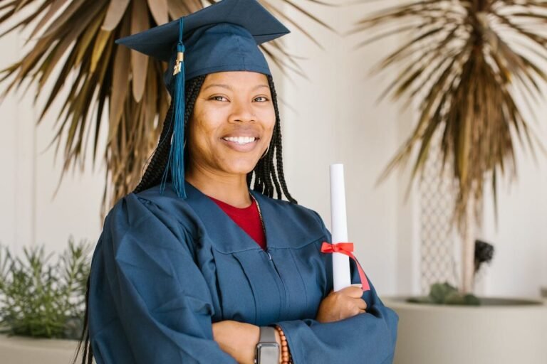 woman in academic gown holding a rolled certificate while smiling at the camera