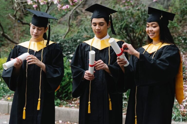 students in graduation gowns and hats unfolding certificates and magnolia in background