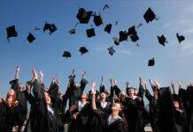newly graduated people wearing black academy gowns throwing hats up in the air