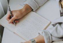 person writing on notebook while holding coffee mug