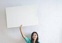 smiling ethnic woman with blank poster in empty flat