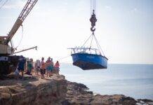 people transporting a boat on crane on rocky coast