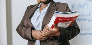 anonymous black female tutor with books standing near whiteboard at school