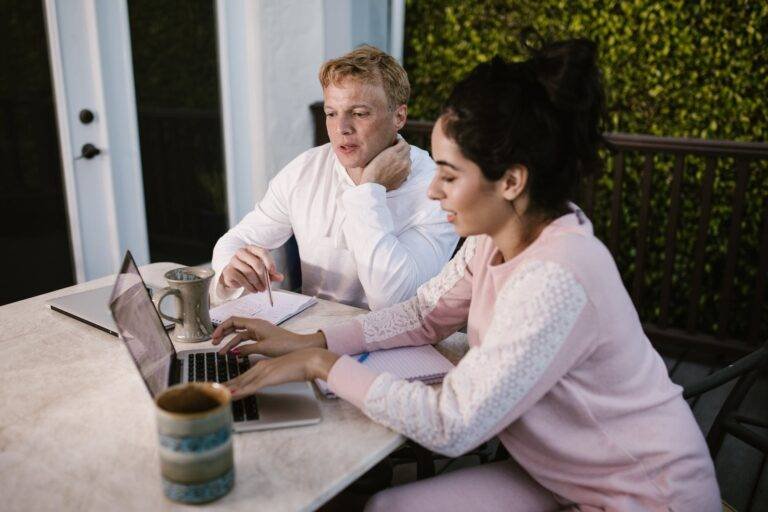 a man and woman sitting near the table with laptop while working together