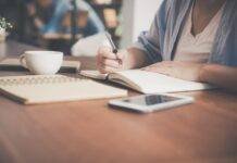 woman writing on a notebook beside teacup and tablet computer