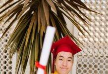 a man wearing red toga and graduation cap holding a rolled certificate while smiling at the camera