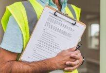 person in yellow reflective safety vest holding a pen and checklist of house inspection