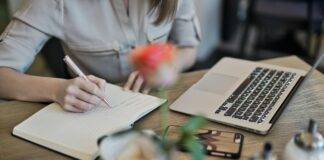 person writing on a notebook beside macbook