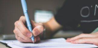 person holding blue ballpoint pen writing in notebook