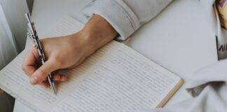 person writing on notebook while holding coffee mug
