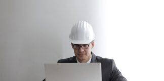 serious engineer working on laptop with blueprints