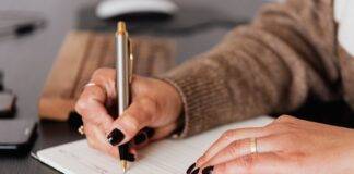 crop woman writing down notes in diary