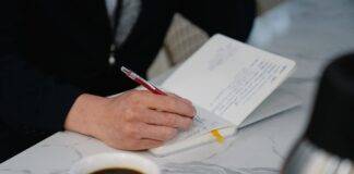 close up of a man writing in his calendar and drinking coffee