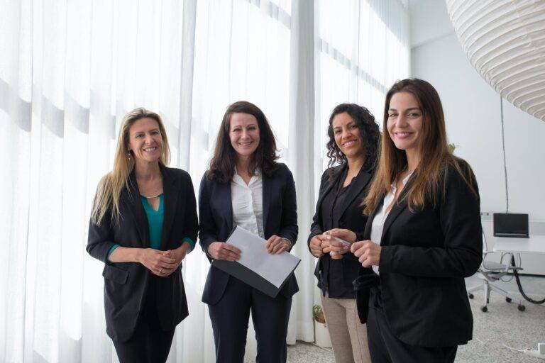 a group of women standing and smiling while wearing corporate attire