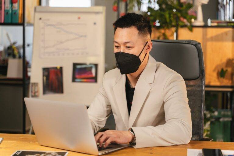 a man in gray blazer wearing face mask while using his laptop