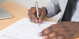 person holding gray twist pen and white printer paper on brown wooden table