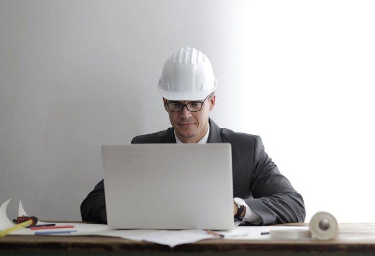 serious engineer working on laptop with blueprints