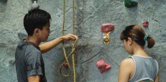 asian trainer explaining to alpinist how to use safety rope