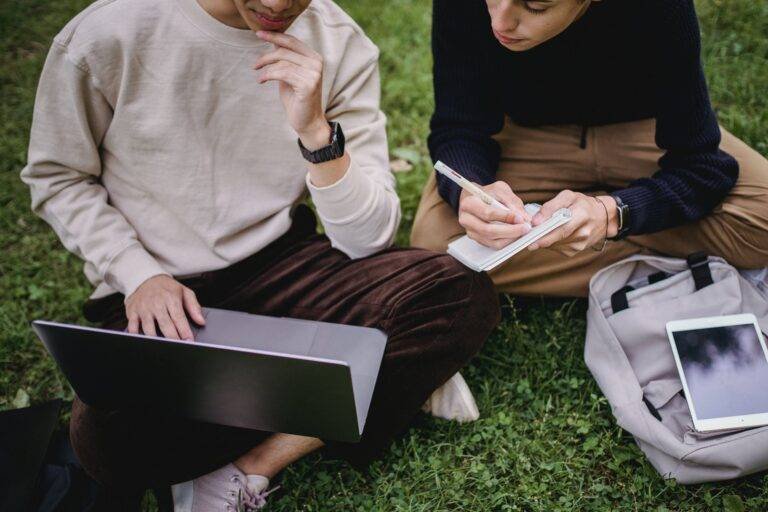 crop ethnic male students using laptop while studying in park