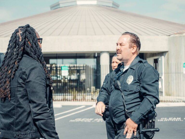 two police officers talking to a man in dreadlocks wearing black jacket
